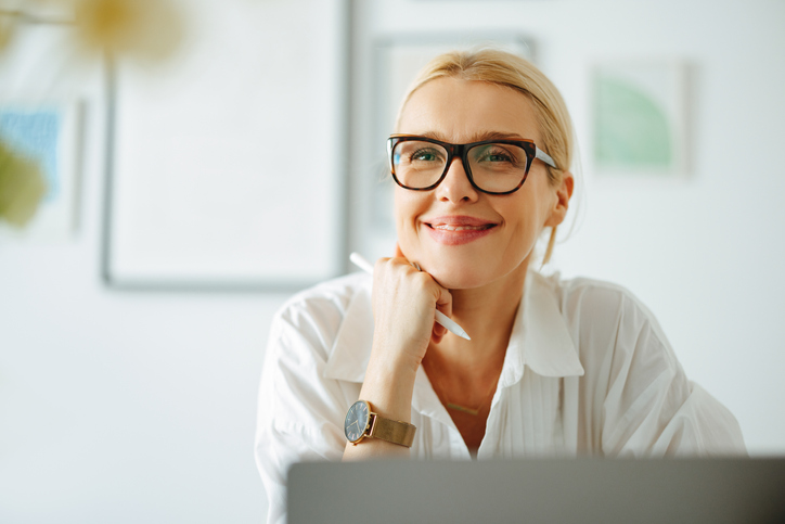 woman in white blouse wearing specs holding a pen